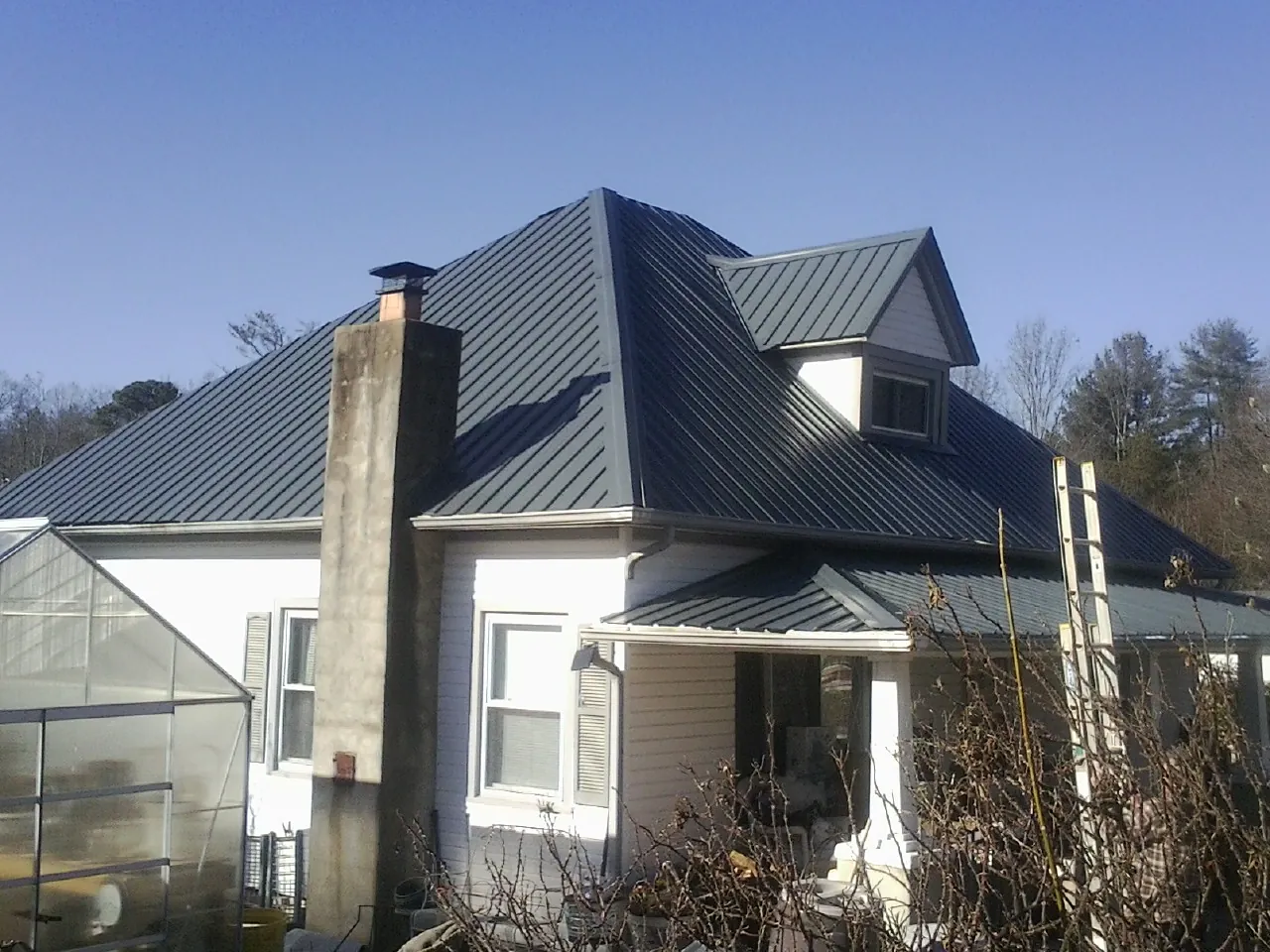 Dark blue standing seam metal roof on a white farmhouse with dormer — Slate & Tile Roof Repair by Roofing Brothers in Maggie Valley
