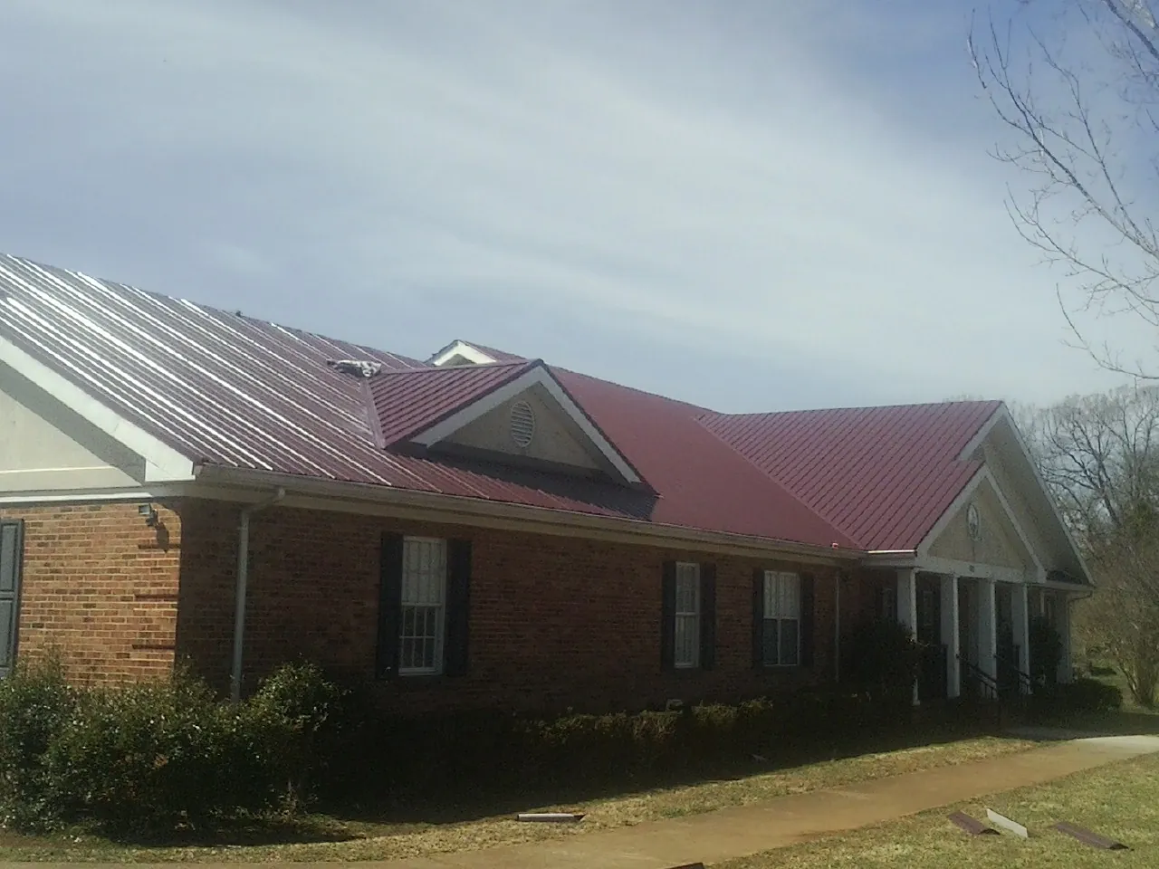 Red metal roof with gabled entries on a long brick building, from a Hail Damage Roof Repair job in Maggie Valley
