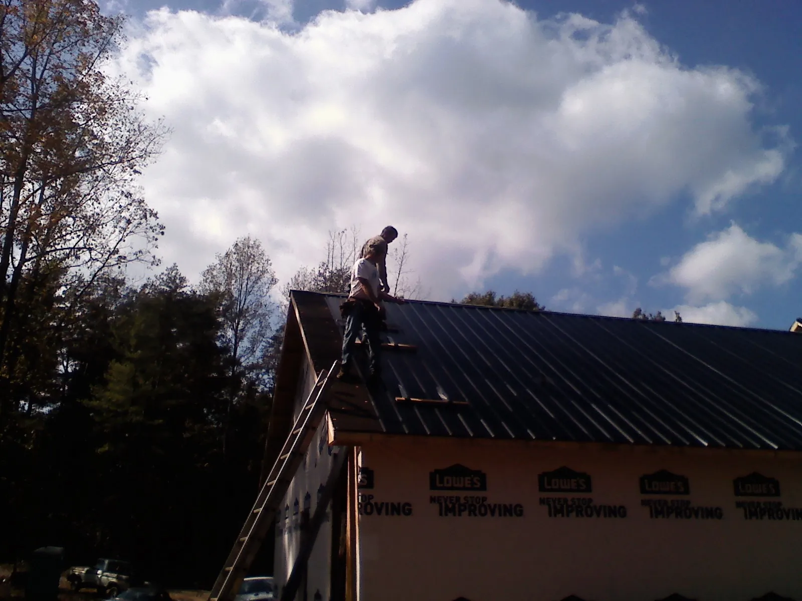 Roofer fastening dark metal panels high against a cloudy sky, from a Roof Inspection job in Maggie Valley