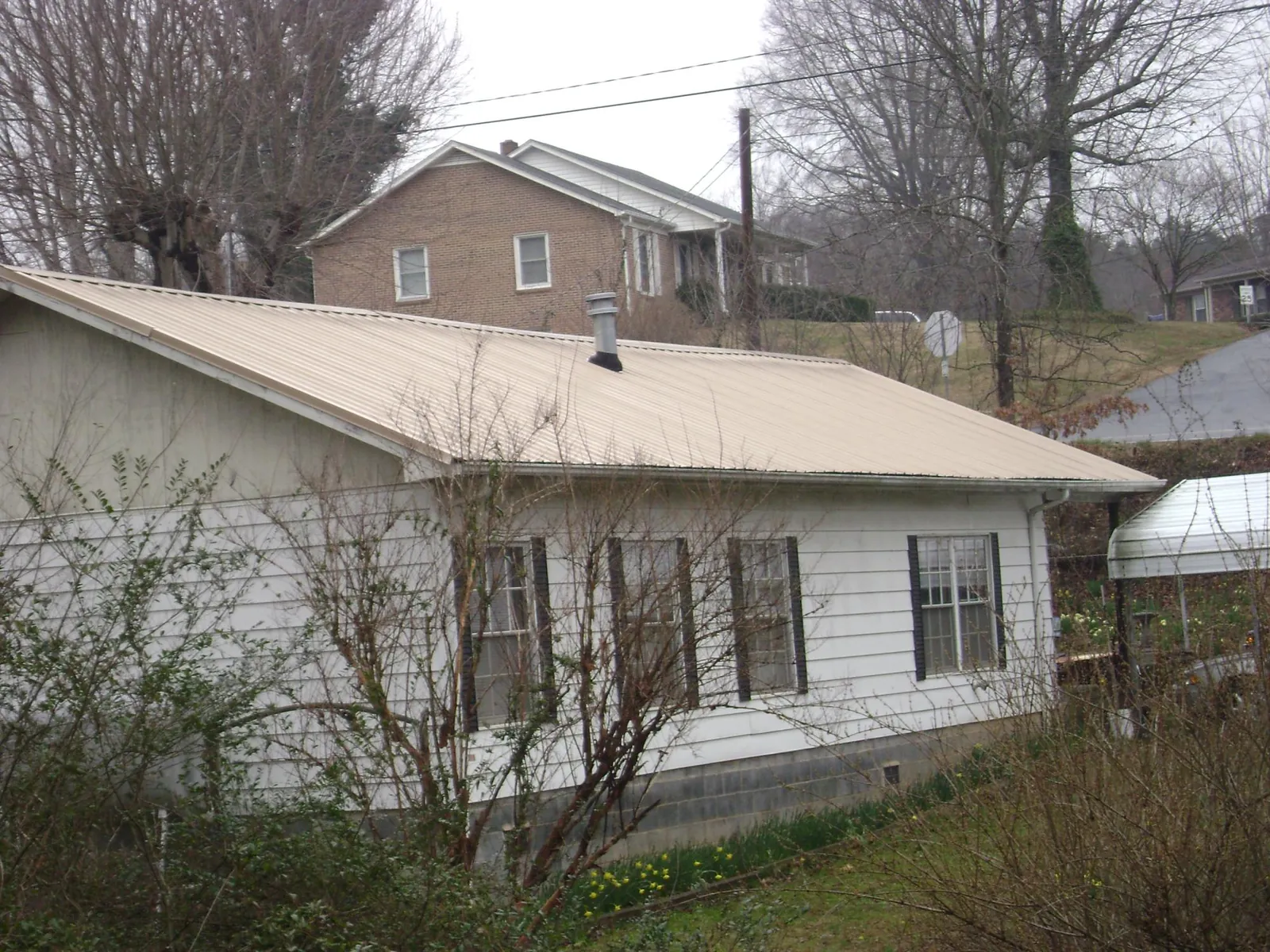 Tan metal roof on a white sided house set into a hillside — Commercial Roofing by Roofing Brothers in Maggie Valley