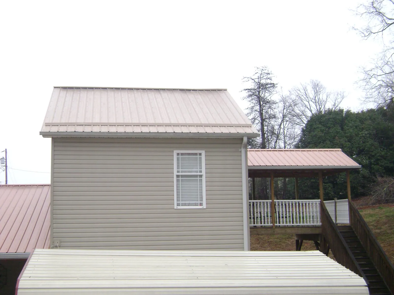 Tan metal roofs on a two story addition and attached porch, from a Roof Replacement job in Maggie Valley