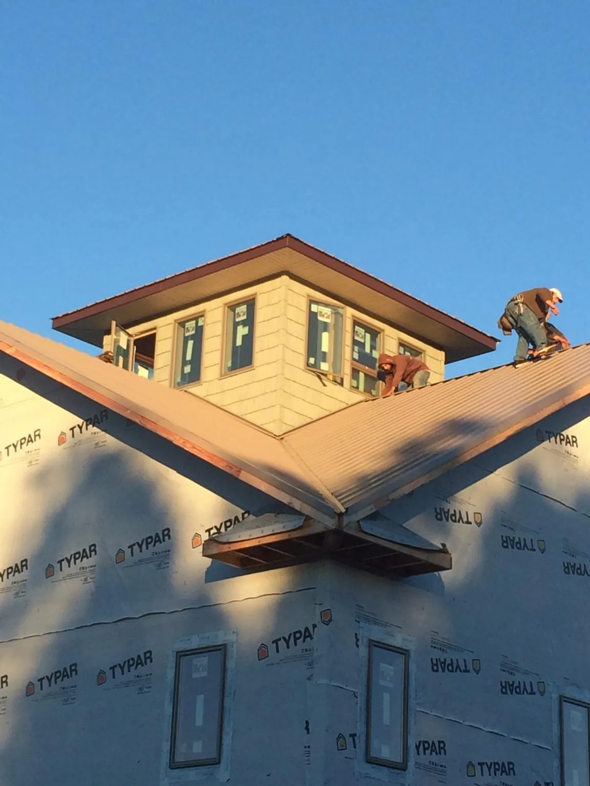 Roofers working around a rooftop cupola on a new metal roof at sunset — Roof Waterproofing in Maggie Valley by Roofing Brothers